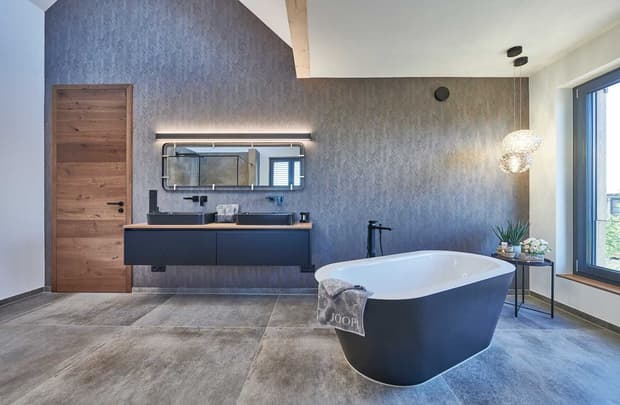 Modernes Badezimmer im Musterhaus mit freistehender Badewanne, Holzdetails, großem Spiegel und stilvoller Beleuchtung.