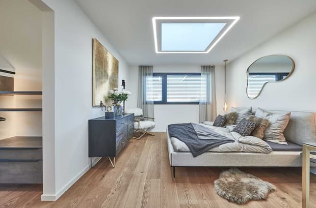 Modernes Schlafzimmer im Musterhaus mit Doppelbett, Holzfußboden, Ankleide, Designleuchte und großem Fenster.