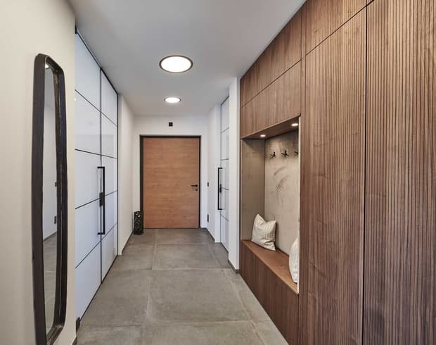Moderner Flur im Musterhaus mit Holzverkleidung, Sitznische, weißen Einbauschränken und stilvoller Beleuchtung.