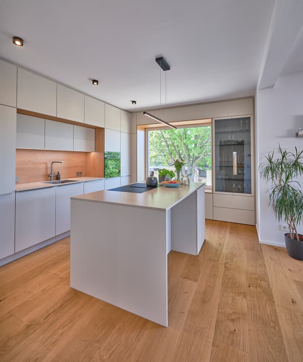 Moderne helle Küche mit weißer Kücheninsel, Holzboden und großem Fenster mit Blick ins Grüne