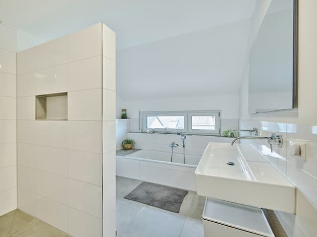 Modernes weiß gekacheltes Badezimmer mit Badewanne, Wandwaschbecken, bodentiefem Fenster und grauer Badezimmermatte