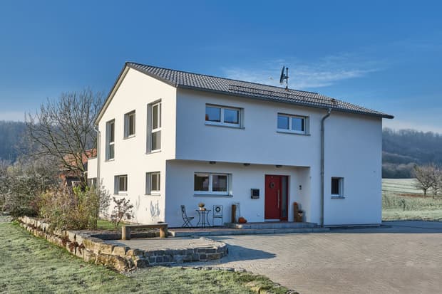 Modernes weißes Einfamilienhaus mit roter Tür, grauem Ziegeldach und kleiner Terrasse an frostigem Wintermorgen