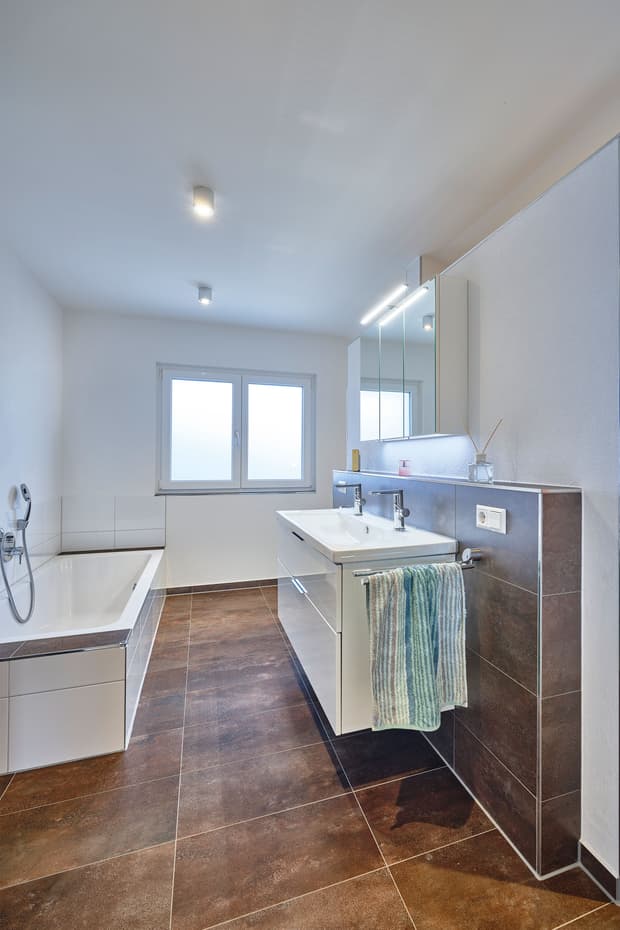 Modernes Badezimmer mit weißer Badewanne, Doppelwaschbecken, braunem Fliesenboden und Badmöbeln in neutralem Design