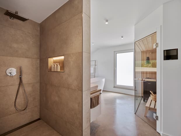 Moderner Wellness-Badezimmerbereich mit brauner Stein-Dusche, freistehender Badewanne und Sauna mit Glastür