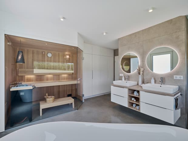 Modernes Badezimmer, integrierte Sauna, Doppelwaschtisch, beleuchtete Rundspiegel, Badewanne und natürliche Holzoptik