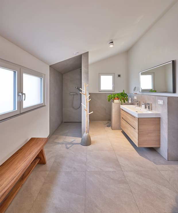 Modernes Badezimmer mit grauen Bodenfliesen, offener Dusche, Holzbank, Waschtisch und Pflanzen