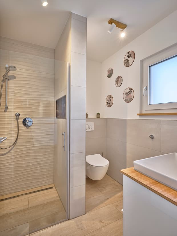 Modernes Badezimmer mit Dusche, hängendem WC, Waschbecken auf Holzplatte und Dekoration an weißer Wand