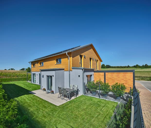 Modernes Einfamilienhaus, Gartenseite, Holzfassade im Obergeschoss, graue Putzfassade, Terrasse, gepflegter Garten und Photovoltaik
