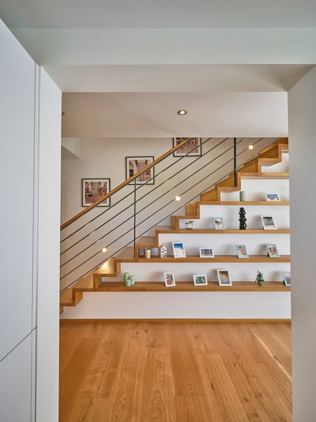 Moderne Holztreppe mit schwarzem Metallgeländer, integrierten Ablageflächen, warmem Holzboden und dekorativen Bilderrahmen