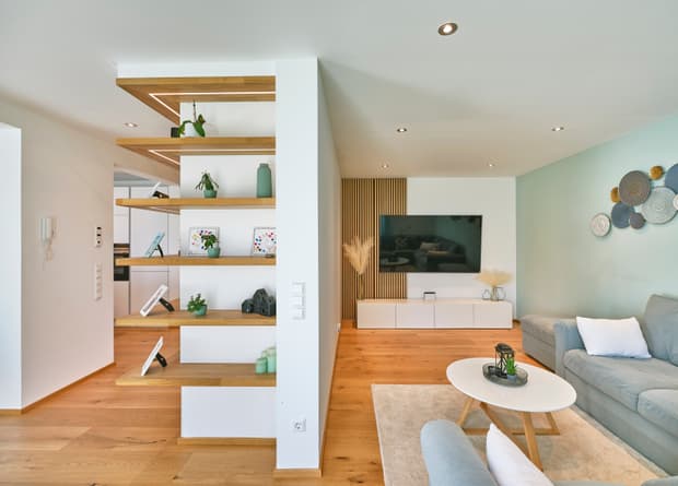 Moderner Wohnraum mit hellblauem Sofa, weißem Couchtisch, offenem Holzregal und TV auf weißer Wand mit Holzvertäfelung