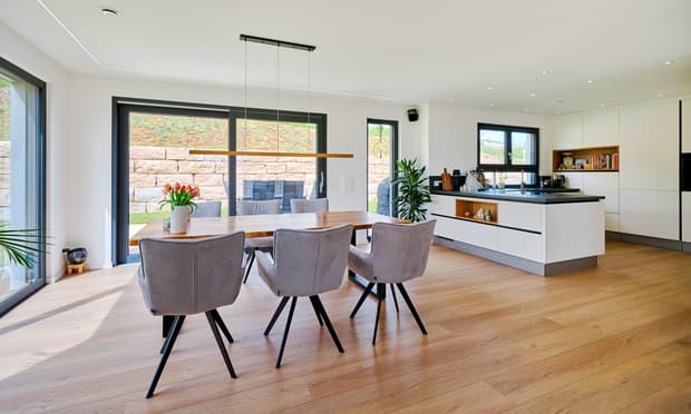 Moderner Essbereich mit Holztisch, grauen Stühlen und offener weißer Küche mit Kochinsel und großem Fenster