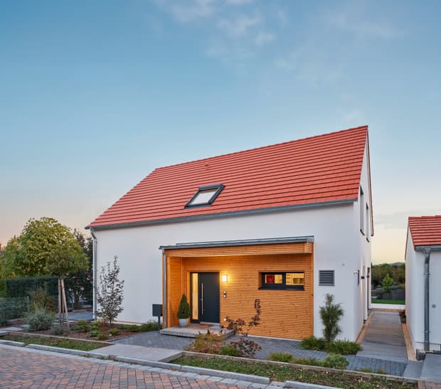 Modernes Einfamilienhaus, weiß verputzte Fassade, rotes Satteldach, Eingangsbereich mit Holzverkleidung, Aufnahme in der Dämmerung