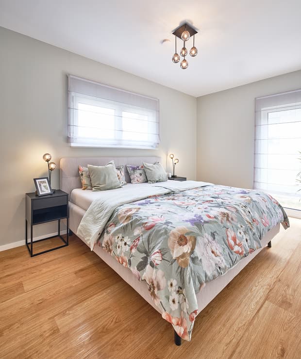 Modernes Schlafzimmer mit Holzboden, hellgrauem Polsterbett und gemusterter Bettdecke mit Blumenmotiven