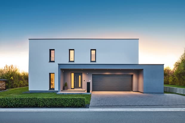 Modernes zweistöckiges Einfamilienhaus mit weißer Fassade, grauer Garage, großem Eingangsbereich und Garten im Abendlicht