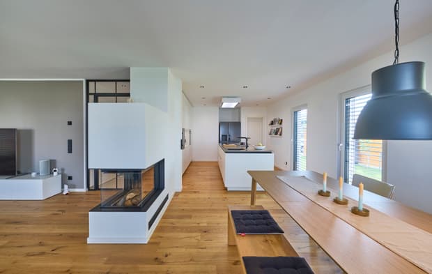 Moderner offener Wohnraum mit hellem Holzboden weiße Küche mit Insel Esstisch mit Bank und Kamin aus Glas und Weiß