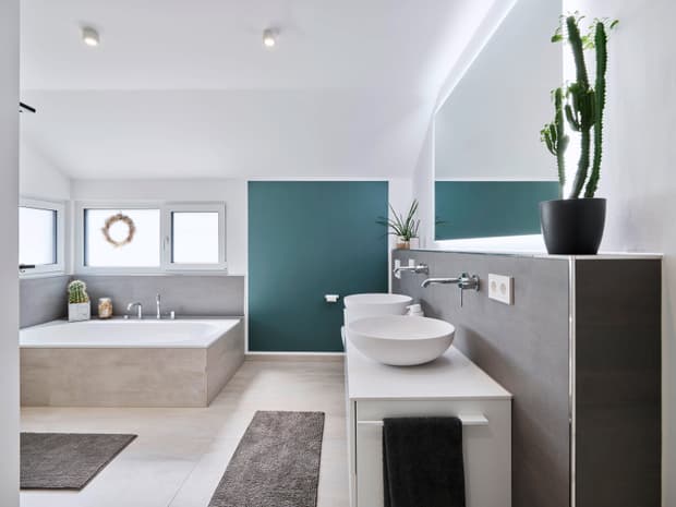 Modernes Badezimmer mit grauer Badewanne, weißen Aufsatzwaschbecken, grüner Akzentwand und Pflanzen im Topf