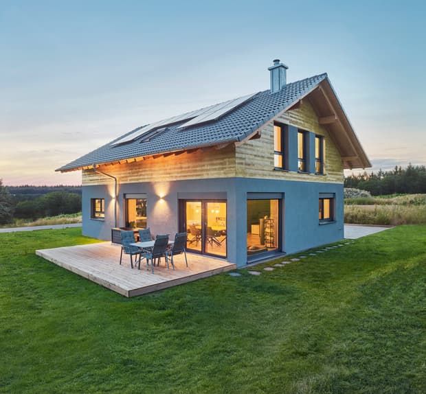 Modernes Einfamilienhaus mit Holz- und Putzfassade, PV-Anlage auf dunklem Ziegeldach, Garten und Terrasse mit Sitzmöbeln