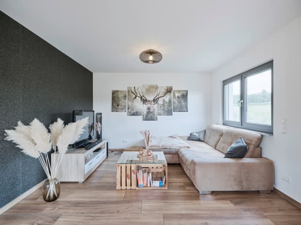 Helles Wohnzimmer mit brauem Samtsofa, Glas-Couchtisch, hellem Holzboden und mehrteiligem Hirschbild an der Wand