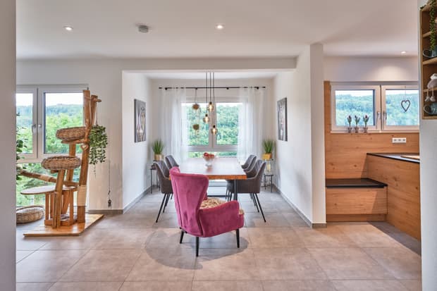 Moderner Essbereich mit Holztisch, grauen Stühlen, pinkem Sessel, großen Fenstern und Katzenspielbaum aus Holz und Korbgeflecht
