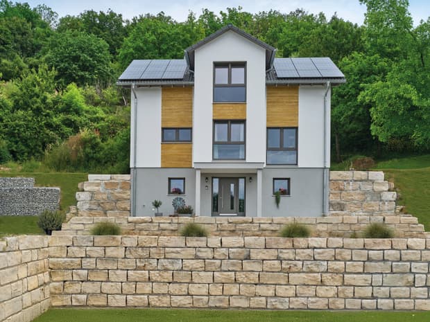 Modernes Einfamilienhaus in Hanglage, weiße Fassade mit Holzdetails, Satteldach mit Photovoltaik und Natursteinmauern