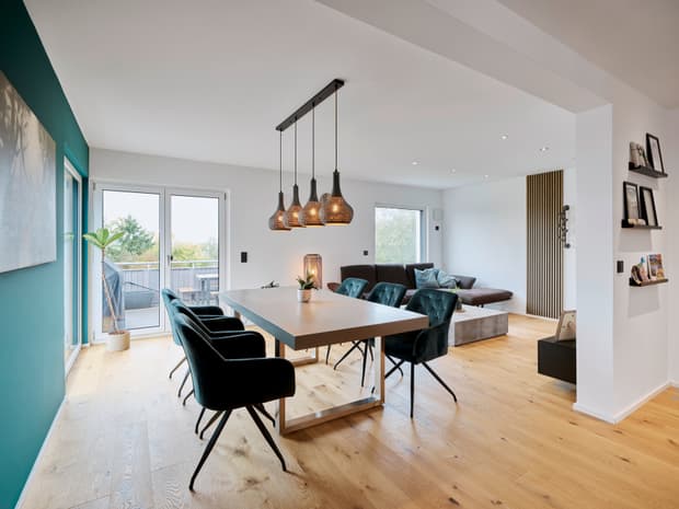 Moderner Essbereich mit hellbraunem Holzboden, grauem Esstisch, dunklen Samtstühlen und Paneel vor weißer Wand im Wohnzimmer