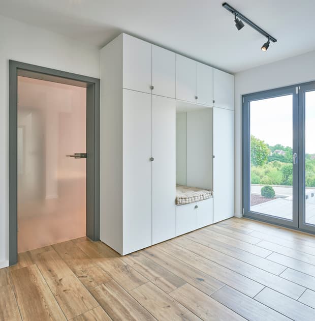 Moderner heller Flur mit Holzoptikfliesen, weißem Einbauschrank mit Sitzbereich und großem Fenster mit Ausblick auf Garten