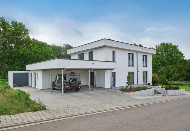 Modernes weißes Einfamilienhaus mit Flachdach, Carport, Garage und begrüntem Grundstück