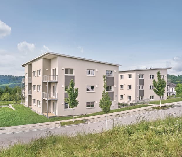 Modernes Mehrfamilienhaus, helle Putzfassade mit grauen Akzenten, Flachdach, Balkone und begrünte Außenanlage