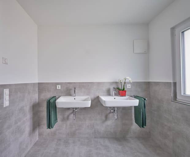 Helles Badezimmer mit zwei Waschbecken, grauen Fliesen, weißen Wänden und großem Fenster