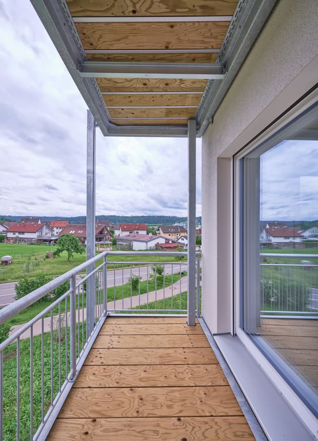 Überdachter Balkon mit Holzboden, Metallgeländer und weitem Blick über die grüne Umgebung