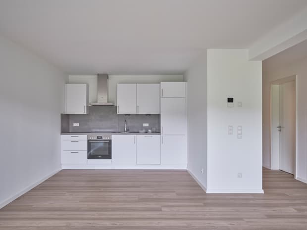 Helle moderne Küche, weiße Fronten, graue Arbeitsflächen, offene Raumgestaltung und Holzoptikboden.