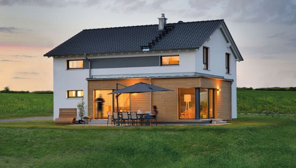 Modernes Fertighaus mit Satteldach und kubischem Anbau bei Abendbeleuchtung