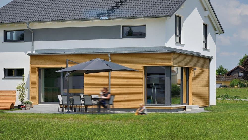 Gemütliche Terrasse mit Sonnenschirm neben dem kubischem Anbau
