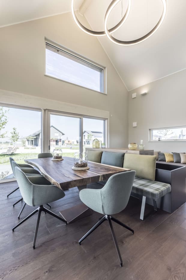 Helles Esszimmer im modernen Musterhaus mit Holztisch, Designstühlen, großer Fensterfront und stilvoller Beleuchtung.