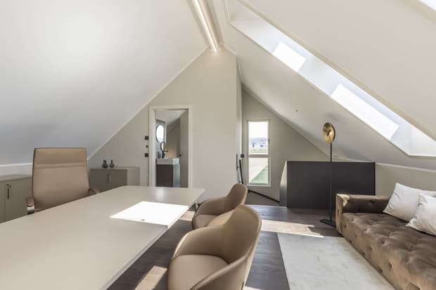 Helles Büro im modernen Musterhaus mit Dachschrägen, großem Schreibtisch, Ledersesseln und gemütlichem Sofa.