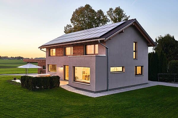 Modernes Einfamilienhaus mit grauem Putz, Holzverkleidung, Solarzellen auf dem Dach und gepflegtem Garten bei Abendlicht