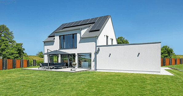 Modernes weißes Einfamilienhaus mit Solarpaneelen auf dem Dach, großer Glasfront und Terrasse im Grünen