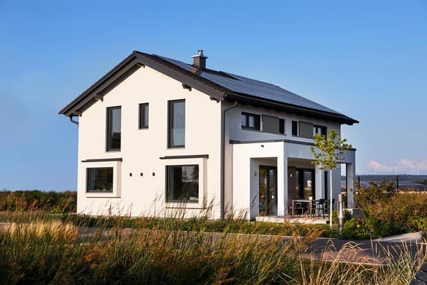 Modernes zweistöckiges Musterhaus mit Satteldach, Solarpanelen, weißer Fassade und großer Terrasse im Grünen.