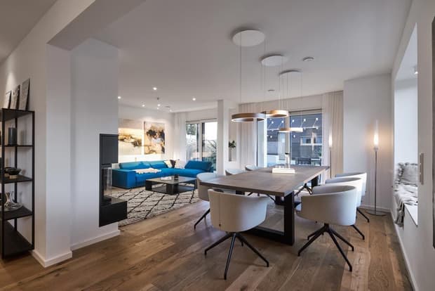 Modernes Musterhaus mit offenem Wohn- und Essbereich, Holzboden, Designmöbeln, Kamin und großen Fenstern.