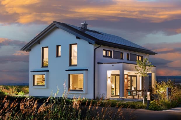 Modernes Musterhaus mit Satteldach, großen Fenstern, Terrasse und energieeffizienter Bauweise bei Sonnenuntergang.