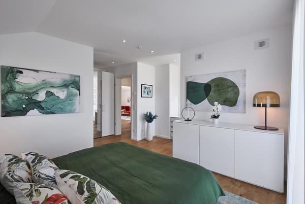 Modernes Musterhaus-Schlafzimmer mit grünem Bett, Holzfußboden, weißer Einrichtung und stilvoller Wandkunst.