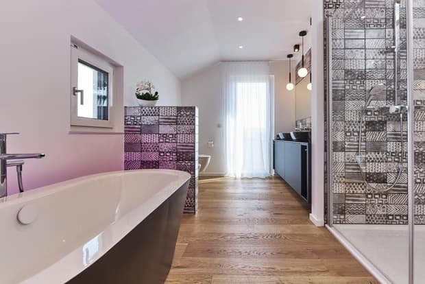 Modernes Badezimmer im Musterhaus mit freistehender Badewanne, Holzfußboden, Glasdusche und stilvollen Fliesen.