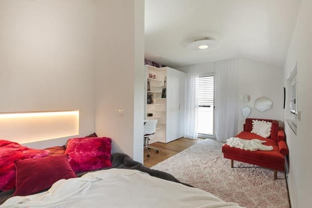 Helles Schlafzimmer im Musterhaus mit rotem Sofa, Bett mit pinken Kissen, Schreibtisch und modernem Design.