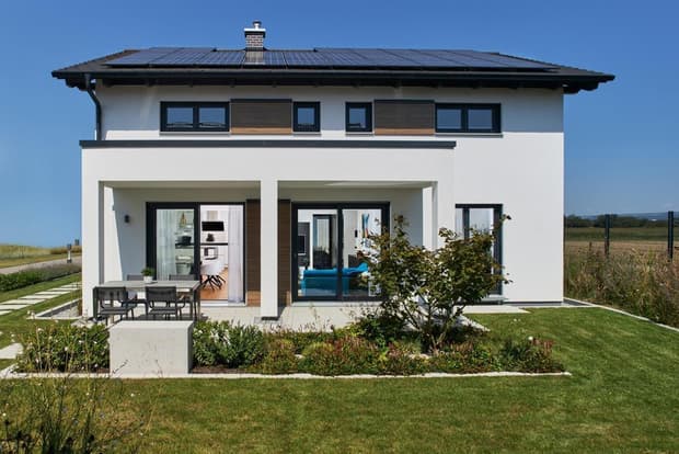 Modernes zweistöckiges Musterhaus mit Solardach, weißer Fassade, Terrasse, Garten und großen Panoramafenstern.