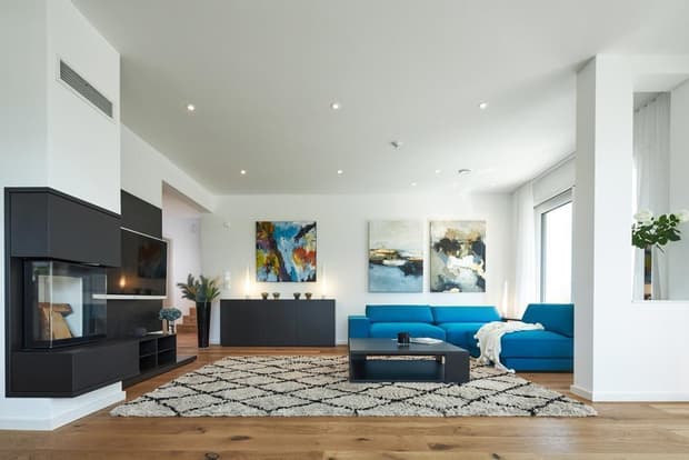 Modernes Musterhaus-Wohnzimmer mit blauer Couch, Kamin, Holzboden, abstrakter Kunst und heller Raumgestaltung.