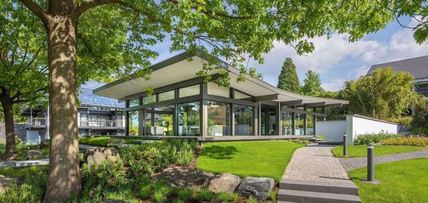 Modernes Haus in Holzständerbauweise mit großen Glasfronten, Flachdach und Garten, zeigt nachhaltige Architektur und energieeffizientes Bauen.