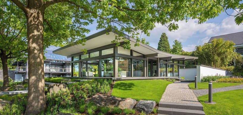 Modernes Haus in Holzständerbauweise mit großen Glasfronten, Flachdach und Garten, zeigt nachhaltige Architektur und energieeffizientes Bauen.