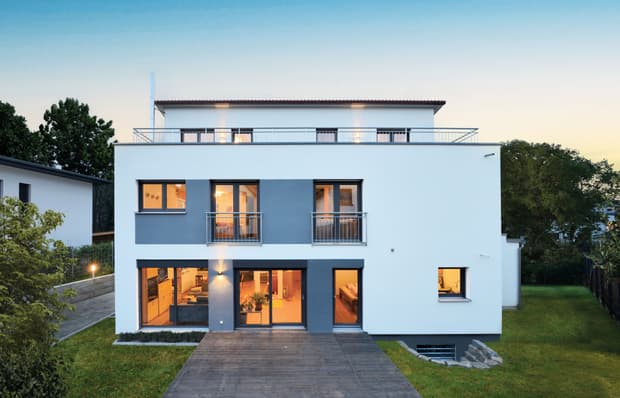 Modernes zweistöckiges Wohnhaus mit weißer Fassade, blauen Fensterrahmen, großem Garten und Terrasse bei Dämmerung