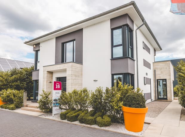 Modernes zweistöckiges Haus mit weißer und grauer Fassade und großem orangefarbenem Blumentopf vor dem Eingang