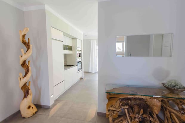 Heller Flur im modernen Musterhaus mit Designmöbeln aus Treibholz, Glasplatte und Blick in offene Küche.